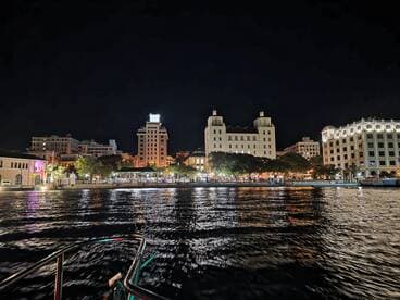 A stunning night view of a vibrant waterfront city, illuminated by colorful lights reflecting on the water — perfect for evening boat tours and sightseeing.