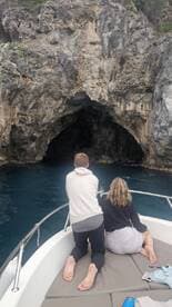 A couple enjoys the stunning view of a cave from the deck of their boat, showcasing the beauty of nature during their adventure.