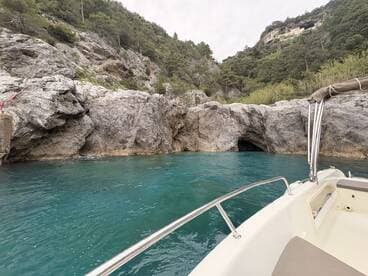 A scenic view of a boat navigating through turquoise waters near a rocky coastline, showcasing the natural beauty of the surroundings.