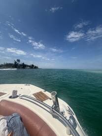 A scenic view from the bow of a boat cruising through clear waters, showcasing the beautiful coastline and blue skies — perfect for a day on the water.