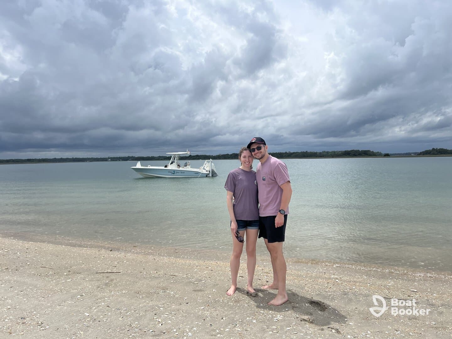 A couple poses on the beach with a boat anchored in the background, capturing a perfect moment of relaxation and adventure by the water.