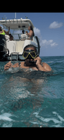 A snorkeler enjoys the vibrant underwater world while a group of friends relaxes on the boat in the background — a perfect day of adventure on the water.