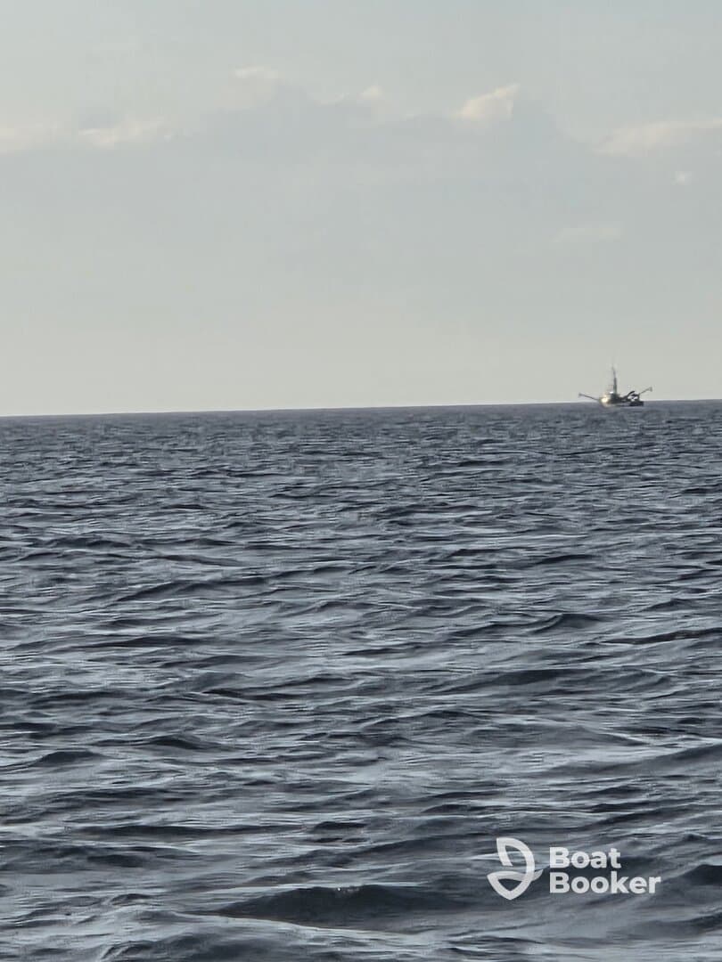 A distant view of a fishing boat navigating through calm waters, showcasing the serene beauty of the open sea.