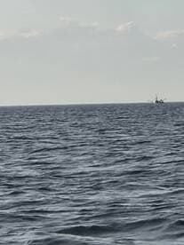 A distant view of a fishing boat navigating through calm waters, showcasing the serene beauty of the open sea.