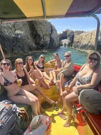 A lively group of friends enjoys a fun day on the water, relaxing on a boat with drinks in hand, surrounded by stunning rock formations — perfect for a memorable celebration.