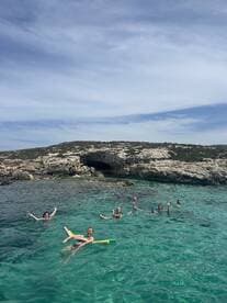 A lively group enjoys a refreshing swim in crystal-clear waters, surrounded by stunning rocky landscapes — perfect for a fun day out on the water.