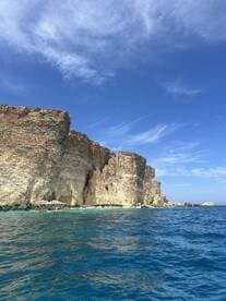 A stunning view of rugged rock formations along the coastline, showcasing the vibrant blue ocean and clear skies — perfect for nature lovers and scenic boat tours.