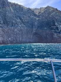 A stunning view of rocky cliffs rising above the sparkling blue ocean, showcasing the natural beauty of the coastline — perfect for adventure seekers exploring by boat.