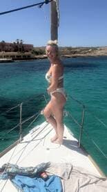 A joyful woman poses on the bow of a boat, enjoying the sunny day and clear turquoise waters — perfect for summer adventures on the sea.