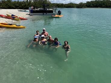 A cheerful group enjoys a refreshing swim in clear waters, surrounded by kayaks and a scenic beach — perfect for a fun day out on the water.
