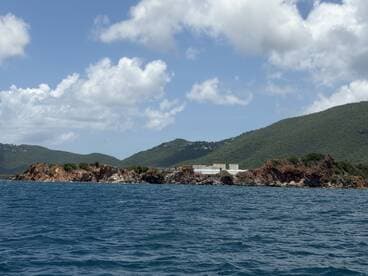 A picturesque view of a rocky coastline with lush green hills in the background, showcasing the natural beauty of the area — perfect for island hopping adventures.