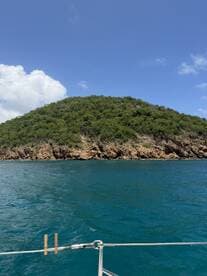 A picturesque view of a lush green island coastline from a boat, showcasing the vibrant blue waters and clear skies — perfect for nature lovers and boating enthusiasts.