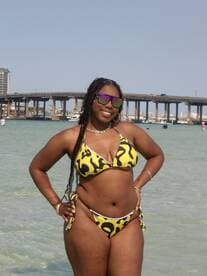 A joyful individual poses on the beach in a vibrant bikini, capturing the essence of a sunny day by the water.