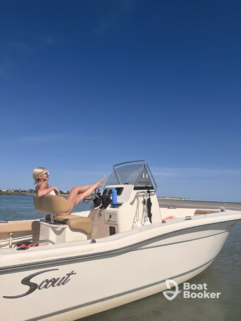 A woman relaxes on the helm of a Scout boat under a clear blue sky, showcasing the perfect day for boating and leisure on the water.
