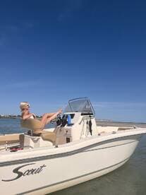 A woman relaxes on the helm of a Scout boat under a clear blue sky, showcasing the perfect day for boating and leisure on the water.