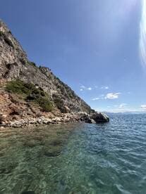 A stunning view of a rocky coastline with crystal-clear waters under a bright blue sky, perfect for showcasing the natural beauty of the area.