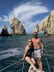 A couple poses joyfully on the bow of a boat, with stunning rock formations in the background — a perfect moment capturing the beauty of Cabo San Lucas.