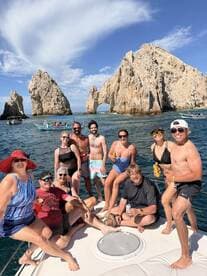 A lively group enjoys a fun day on the water near Cabo San Lucas, celebrating with drinks and laughter against a stunning rock formation backdrop.