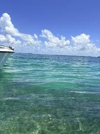 A serene view of a boat's side gliding through crystal-clear waters under a bright blue sky, perfect for showcasing the beauty of a day on the water.