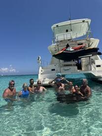 A joyful group enjoys a refreshing swim in crystal-clear waters, with a boat anchored nearby, perfect for family outings and fun on the water.