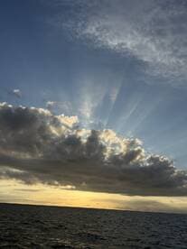 A scenic view of clouds and rays of sunlight over the ocean, creating a tranquil atmosphere.