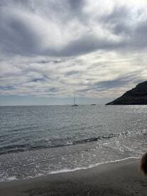 A serene view of a sailboat anchored in calm waters, framed by a picturesque beach and cloudy skies — perfect for a tranquil day on the water.