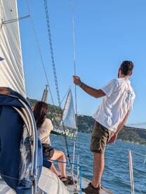 A group enjoys a sailing experience on the water, with another sailboat visible in the background, capturing the essence of adventure and camaraderie.
