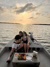 A couple celebrates a birthday on a boat at sunset, enjoying cocktails and a beautifully arranged platter of snacks — a perfect romantic getaway on the water.
