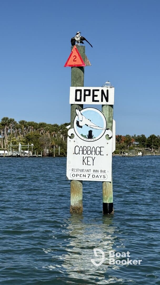 A sign for Cabbage Key, indicating it's open for business, with a scenic waterfront backdrop. Ideal for visitors seeking dining and relaxation options in a picturesque setting.