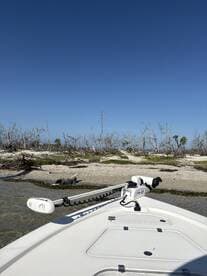 A clear view of the front of a boat anchored near a sandy shore, showcasing the vessel's structure against a bright blue sky.