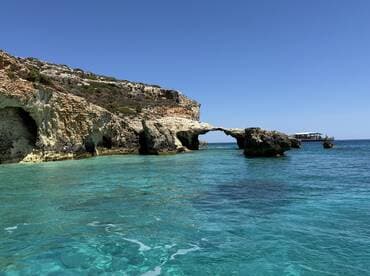 A stunning view of a natural rock formation arching over crystal-clear turquoise waters, showcasing the beauty of the coastline — perfect for scenic boat tours and exploration.