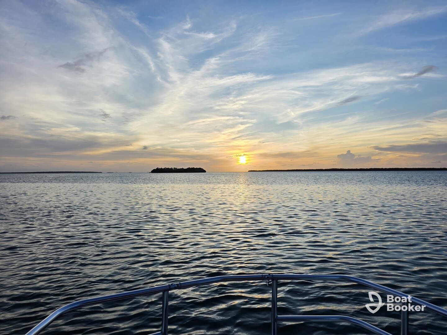 A serene sunset view from the bow of a boat, showcasing calm waters and a distant island — perfect for tranquil evening cruises.