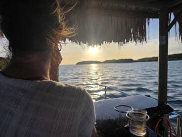 A serene sunset view from a boat, featuring a guest enjoying the moment with a drink in hand — perfect for capturing the essence of relaxation on the water.