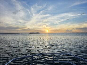 A serene sunset view from the bow of a boat, showcasing calm waters and a distant island — perfect for tranquil evening cruises.