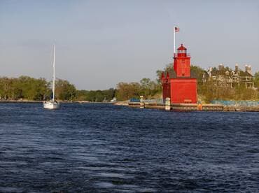 A serene view of a sailboat navigating past a vibrant red lighthouse, showcasing the beauty of coastal scenery and maritime architecture.