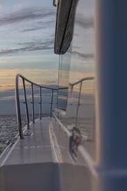 A sleek view of a boat's side railing reflecting the serene colors of the sky at sunset, showcasing the beauty of being underway on the open water.
