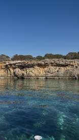 A stunning view of a rocky coastline reflected in the crystal-clear waters, showcasing the natural beauty of the area — perfect for scenic boat trips.