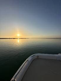A serene sunset view from the bow of a boat, showcasing calm waters and a picturesque horizon — perfect for evening cruises.