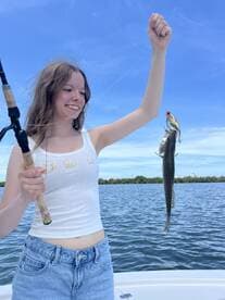 A young girl proudly holds up her catch while fishing on a boat, showcasing the joy of outdoor adventures and fishing experiences.