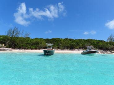 Two boats anchored in crystal-clear turquoise waters, showcasing a serene beach setting perfect for a day of relaxation and exploration.