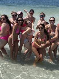 A lively group of friends enjoys a fun day at the beach, celebrating with drinks and laughter in the shallow waters — perfect for bachelorette parties or summer getaways.