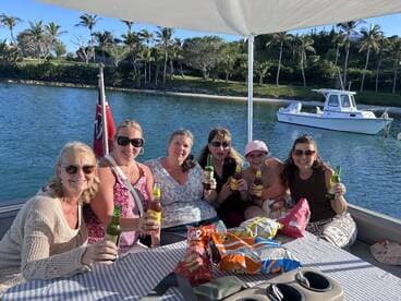 A lively group of friends enjoys drinks and snacks aboard a pontoon boat, celebrating together in a picturesque waterfront setting.