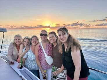 A joyful group of friends poses together on a yacht at sunset, capturing a perfect moment of celebration and camaraderie on the water.