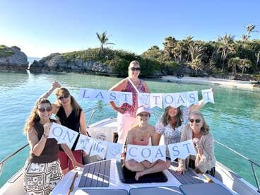 A joyful group of friends celebrates with a 'Last Toast on the Coast' banner aboard a boat, surrounded by stunning coastal scenery — perfect for memorable gatherings and celebrations.