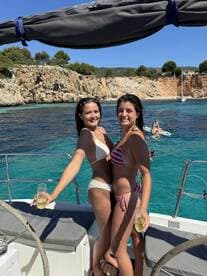 Two friends celebrate on the deck of a yacht with cocktails, enjoying a sunny day by the beautiful turquoise waters — perfect for summer adventures.