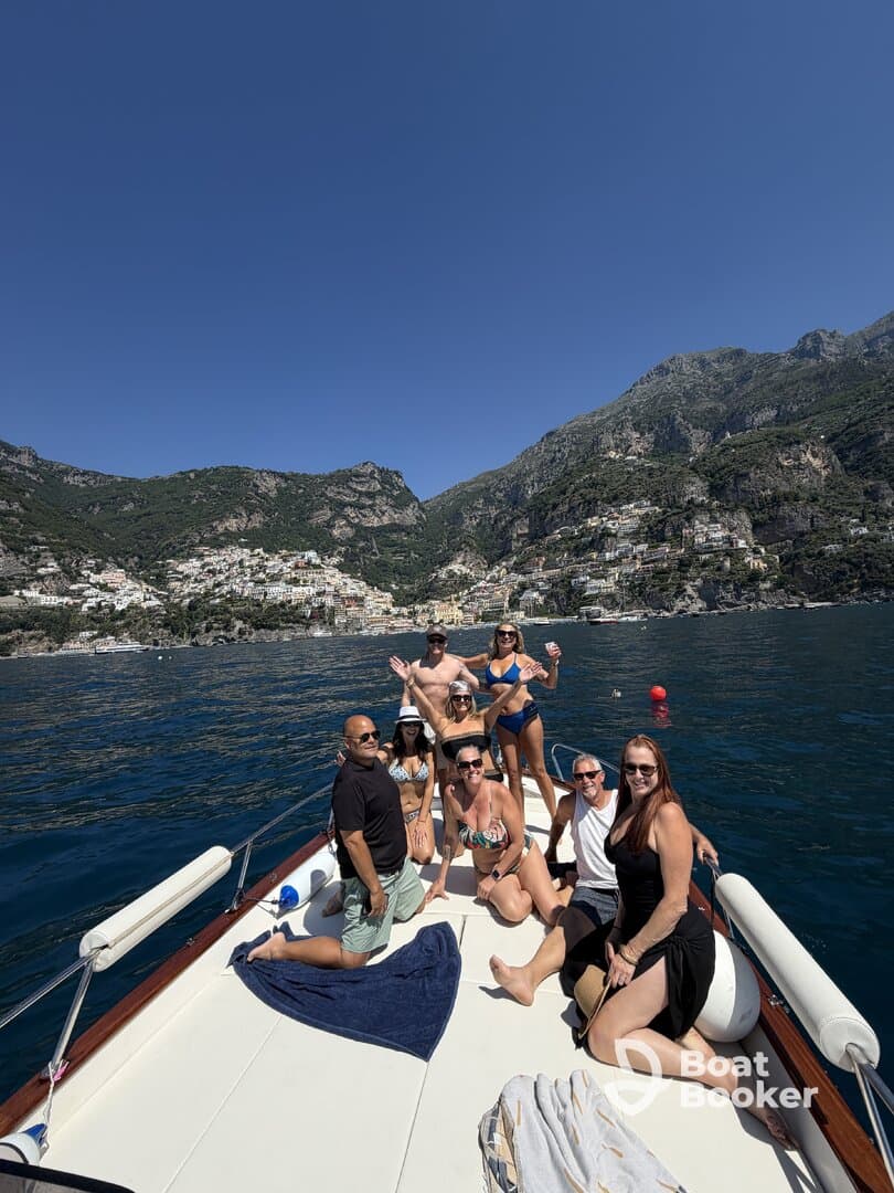 A lively group enjoys a day on the water, posing on the deck of a boat with stunning coastal views in the background — perfect for summer adventures and celebrations.