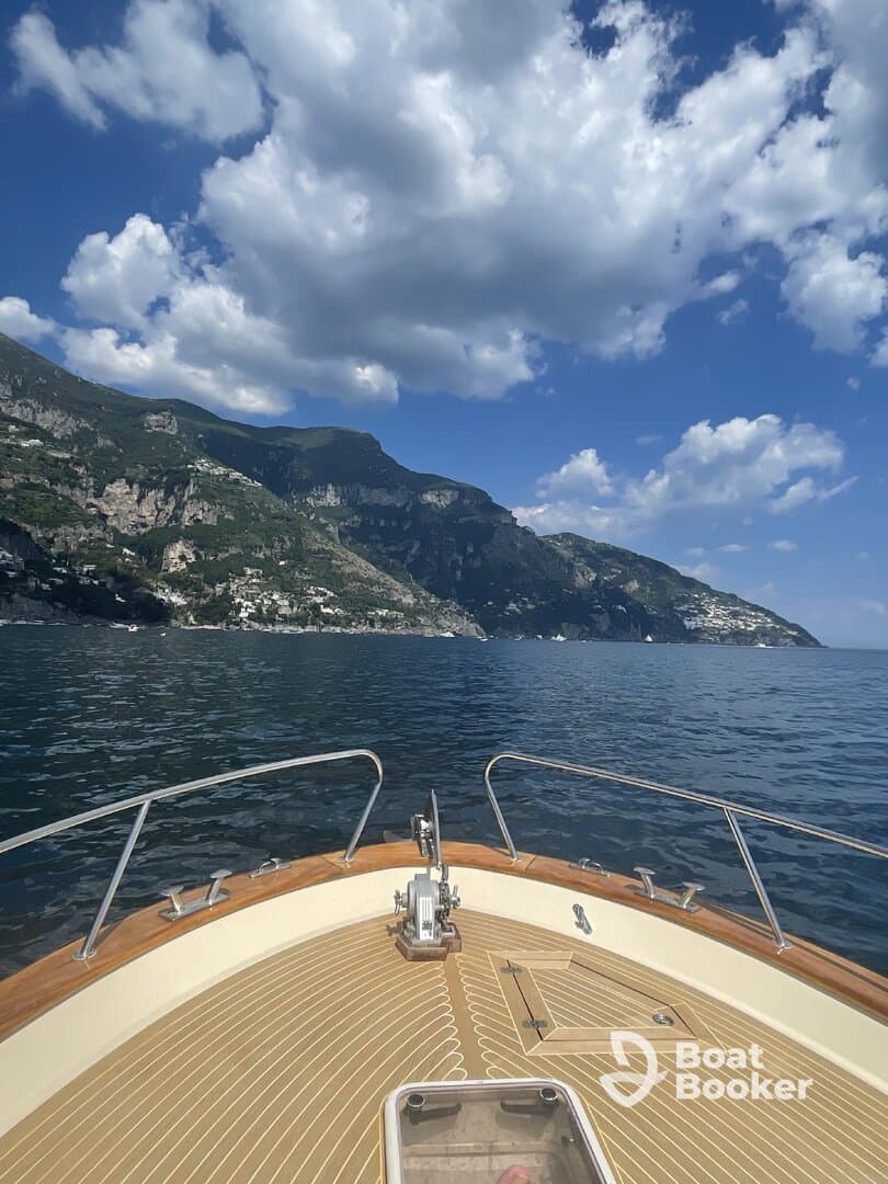 A stunning view from the bow of a boat, showcasing the beautiful coastline and dramatic mountains under a bright blue sky — perfect for exploring scenic destinations.