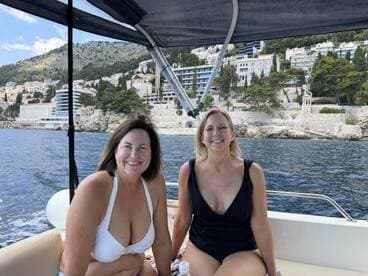 Two friends enjoy a sunny day on a boat, smiling against a picturesque coastal backdrop — perfect for memorable outings and adventures on the water.