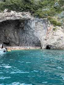 A vibrant scene at a secluded beach with groups of people enjoying the clear waters and exploring the nearby cave — a perfect spot for relaxation and adventure.