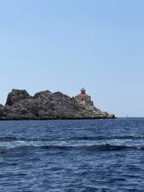 A picturesque view of a lighthouse perched on rocky cliffs, surrounded by tranquil waters — a stunning landmark perfect for boat tours and scenic cruises.